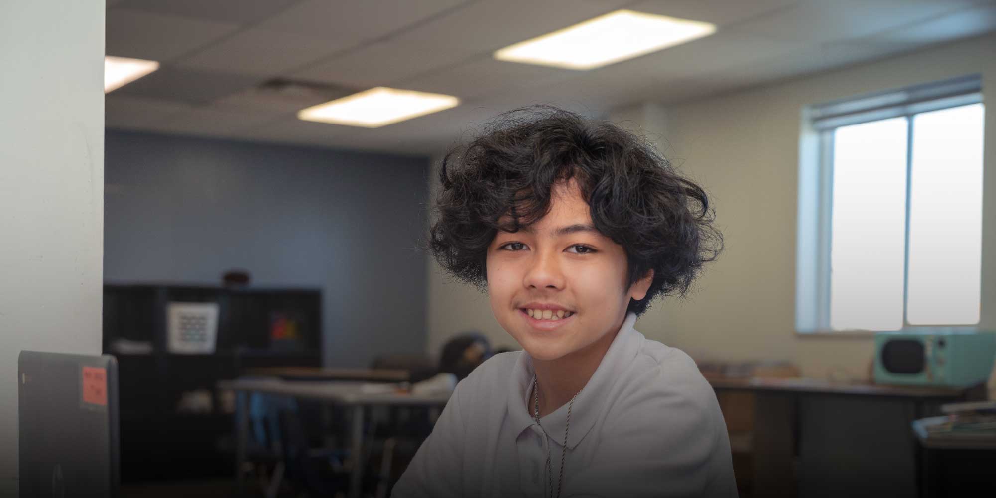 Smiling student with curly hair in a classroom.