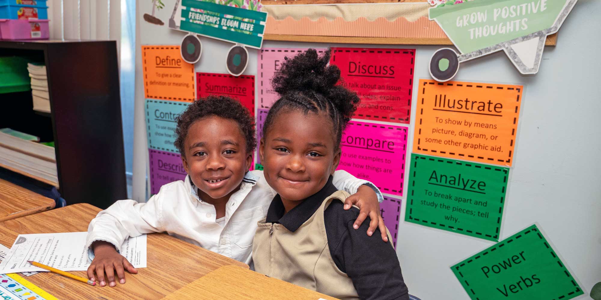 Two smiling students sitting together at a classroom desk.